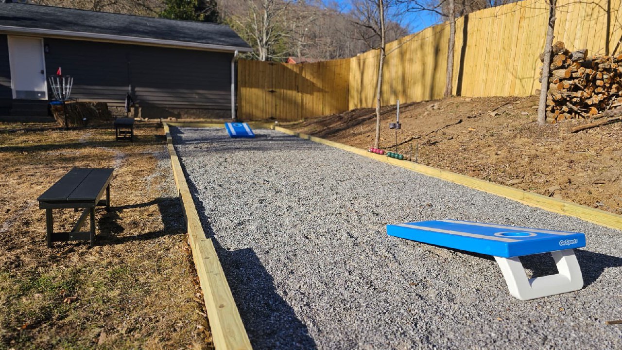 Bocce and cornhole court with disc golf basket in fenced backyard